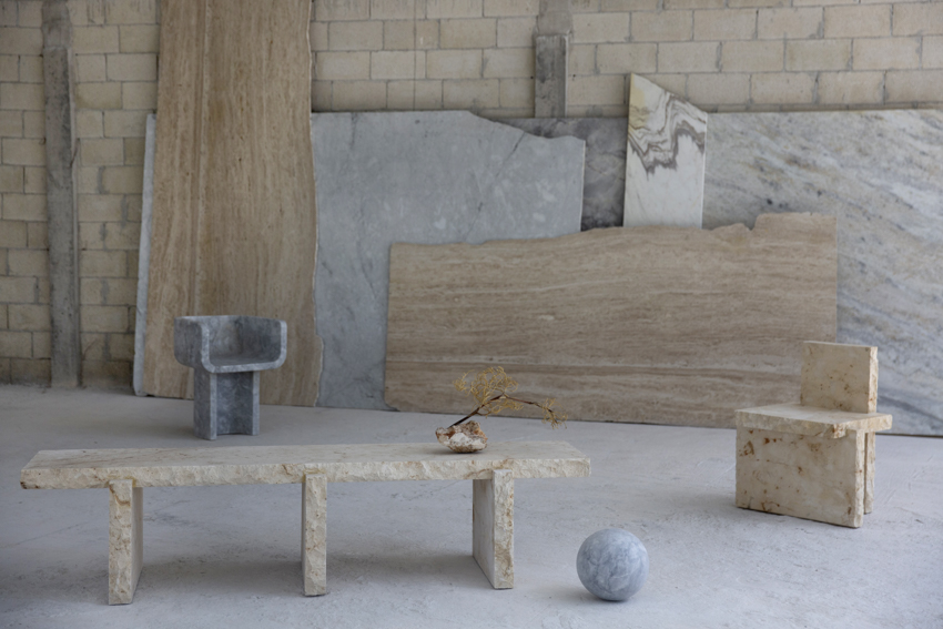 Bench 20 in front of leaning stone slabs, with Chair 11 in grey marble and Chair 20 in limestone behind