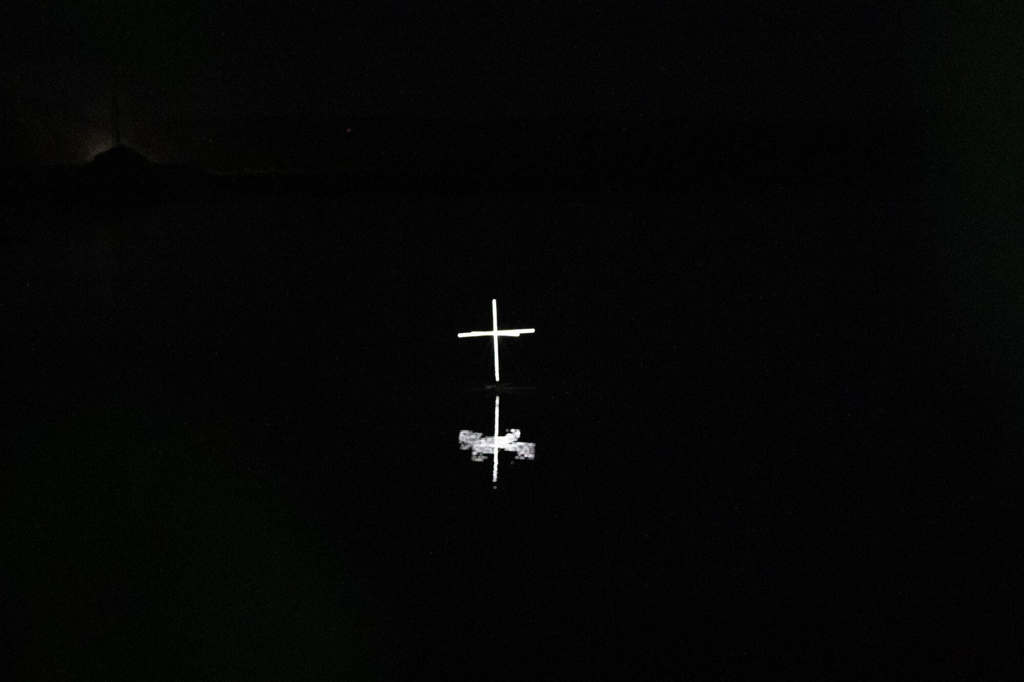 The cross of light from further away, hills faint behind