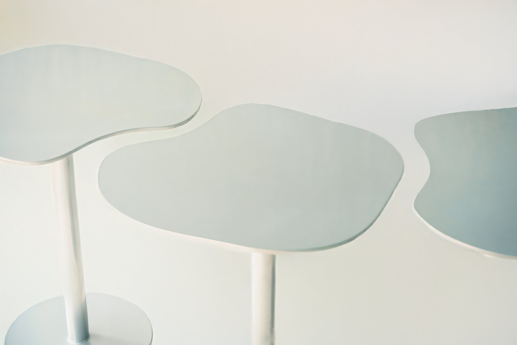 Three steel tables with irregular rounded tops seen from above, their edges almost meeting