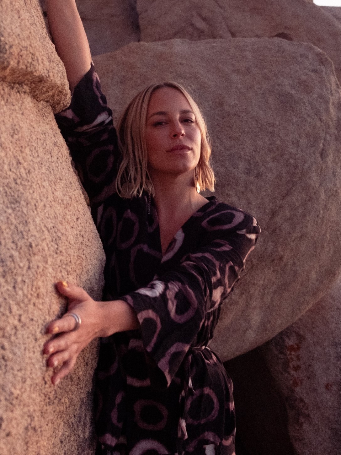 Steffi Ström between granite boulders at dusk, one hand pressed flat against the stone