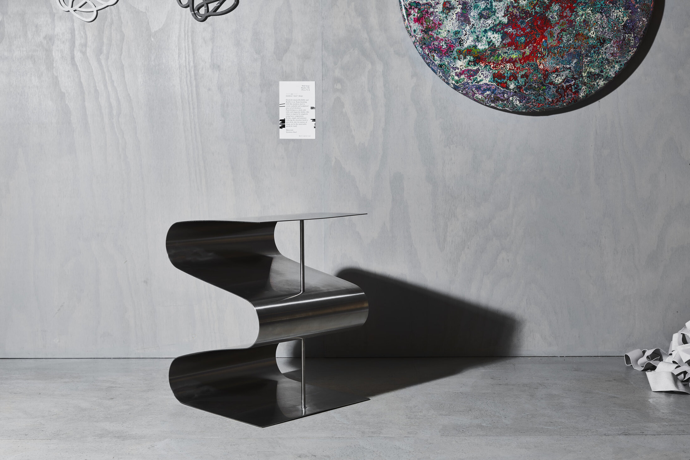 Elasticity Sculpture on the gallery floor beside its wall label, a large painted disc above